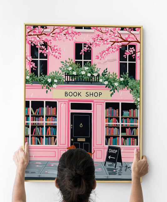 Dachshund in red polka dot sweater standing in front of pink bookshop with cherry blossoms and books