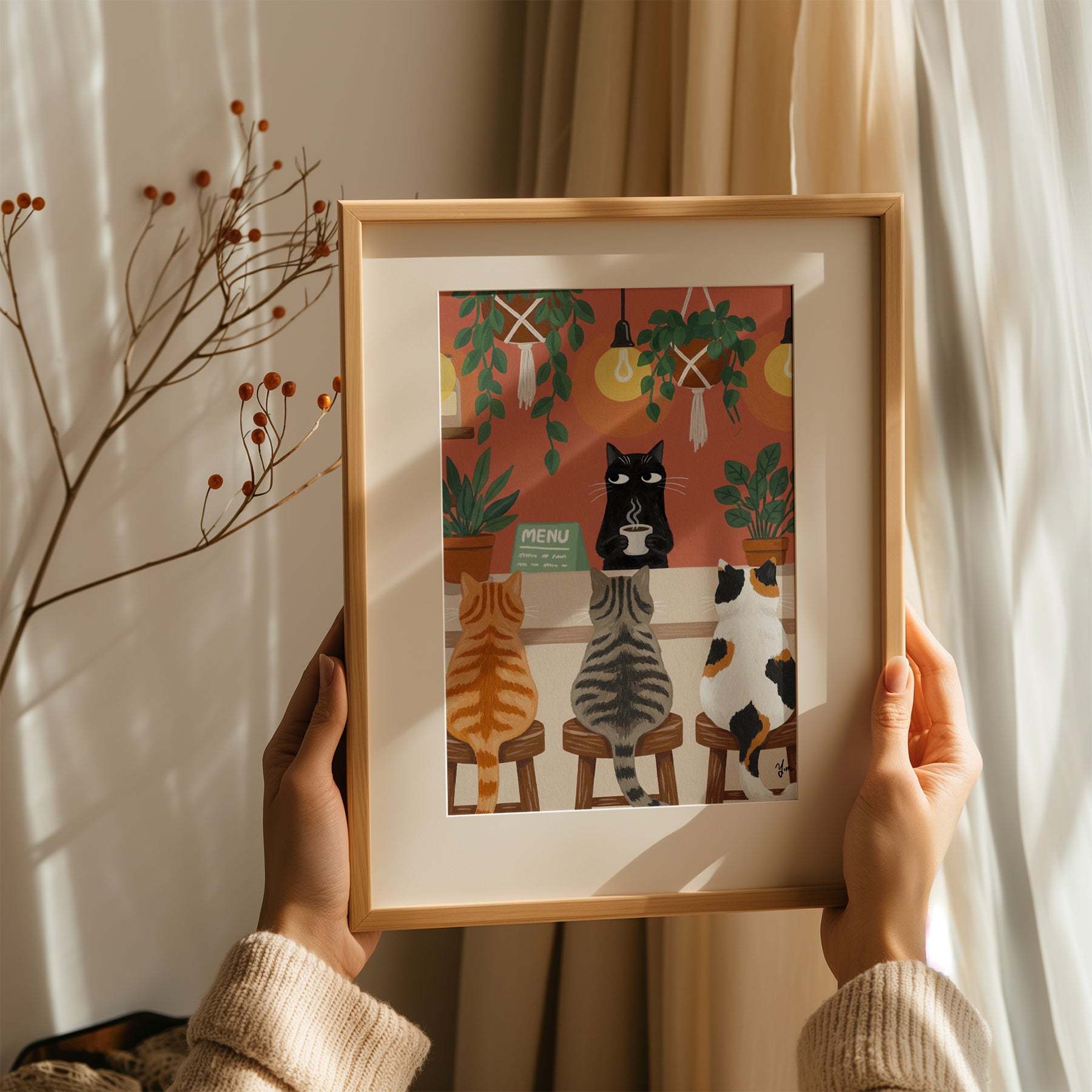 A whimsical illustration of a cozy cat café scene where three cats—a ginger tabby, a gray striped tabby, and a calico—sit on wooden stools at a coffee bar. A black cat barista stands behind the counter holding a steaming cup of coffee. The café is warmly lit with glowing hanging bulbs and decorated with lush green potted and hanging plants. The background features an earthy orange-red wall, creating a comforting and inviting atmosphere.