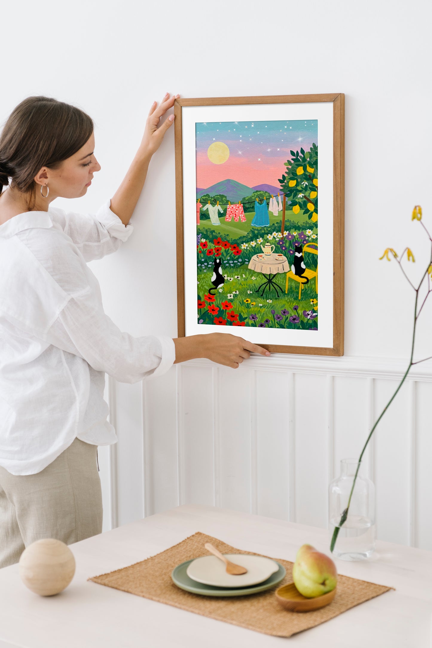 Two cats having tea at sunset with a laundry line in the background and a whimsical landscape scene perfect for cozy home wall decor

